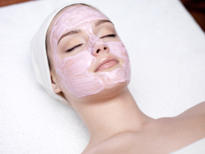 Beautiful young woman with pink facial mask in spa salon - indoors